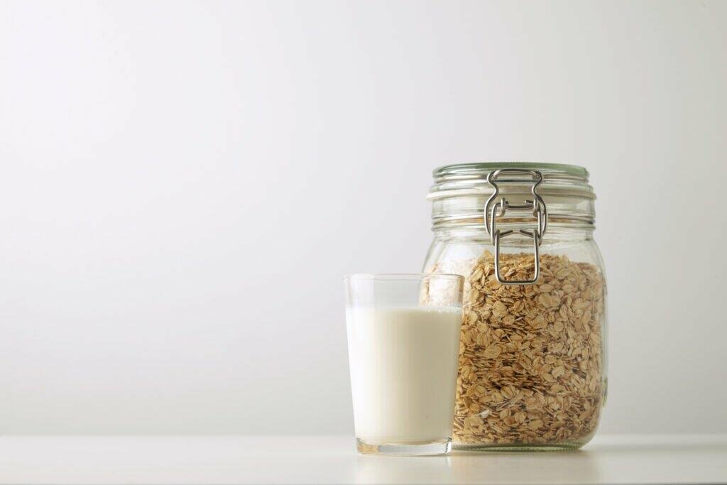 transparent glass with fresh organic milk close rustic jar with rolled oats isolated side white table