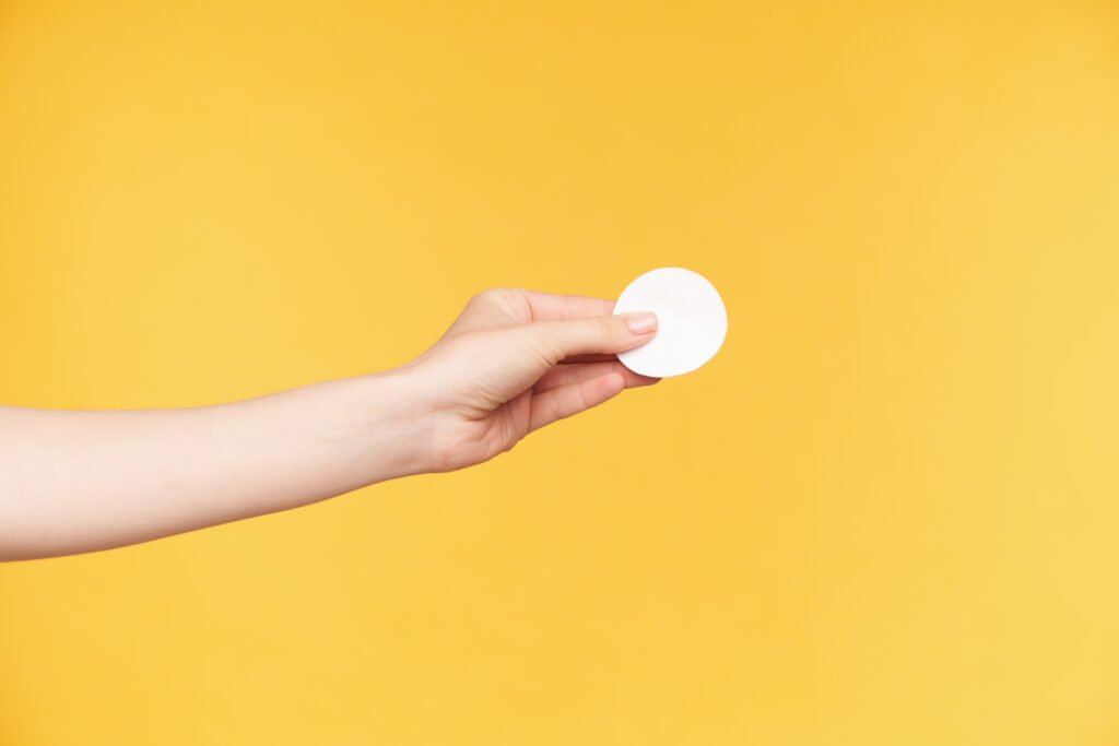 studio photo young well groomed female s hand holding round cotton pad while going wash out make up from face isolated orange background